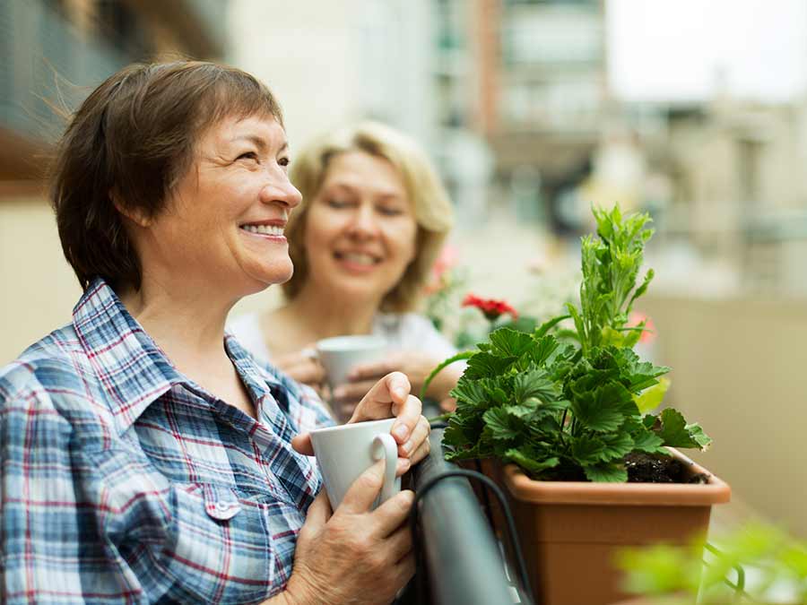 Patients wearing hearing aids from True Tone Hearing in Northern Ireland chat over coffee on a balcony