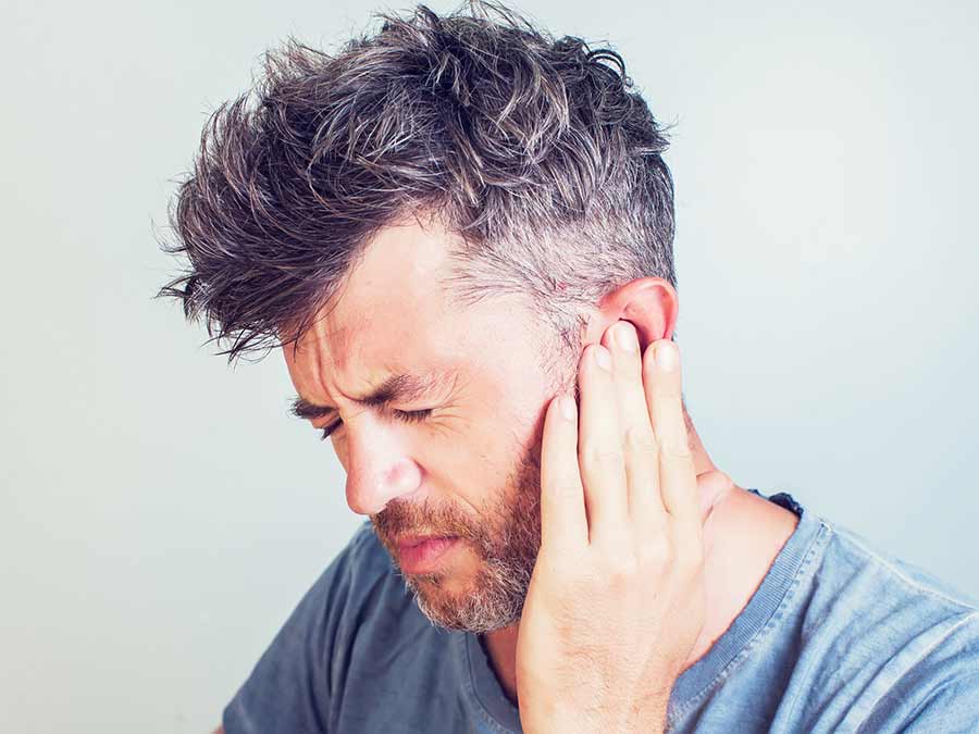 A male suffering with ear pain holds his ear