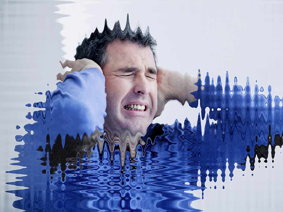 Causes of tinnitus - here a blurred image of a man holding his ears is used to represent the feeling that tinnitus causes